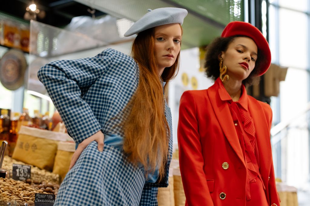 Two stylish women in blazers and berets posing elegantly in a market.